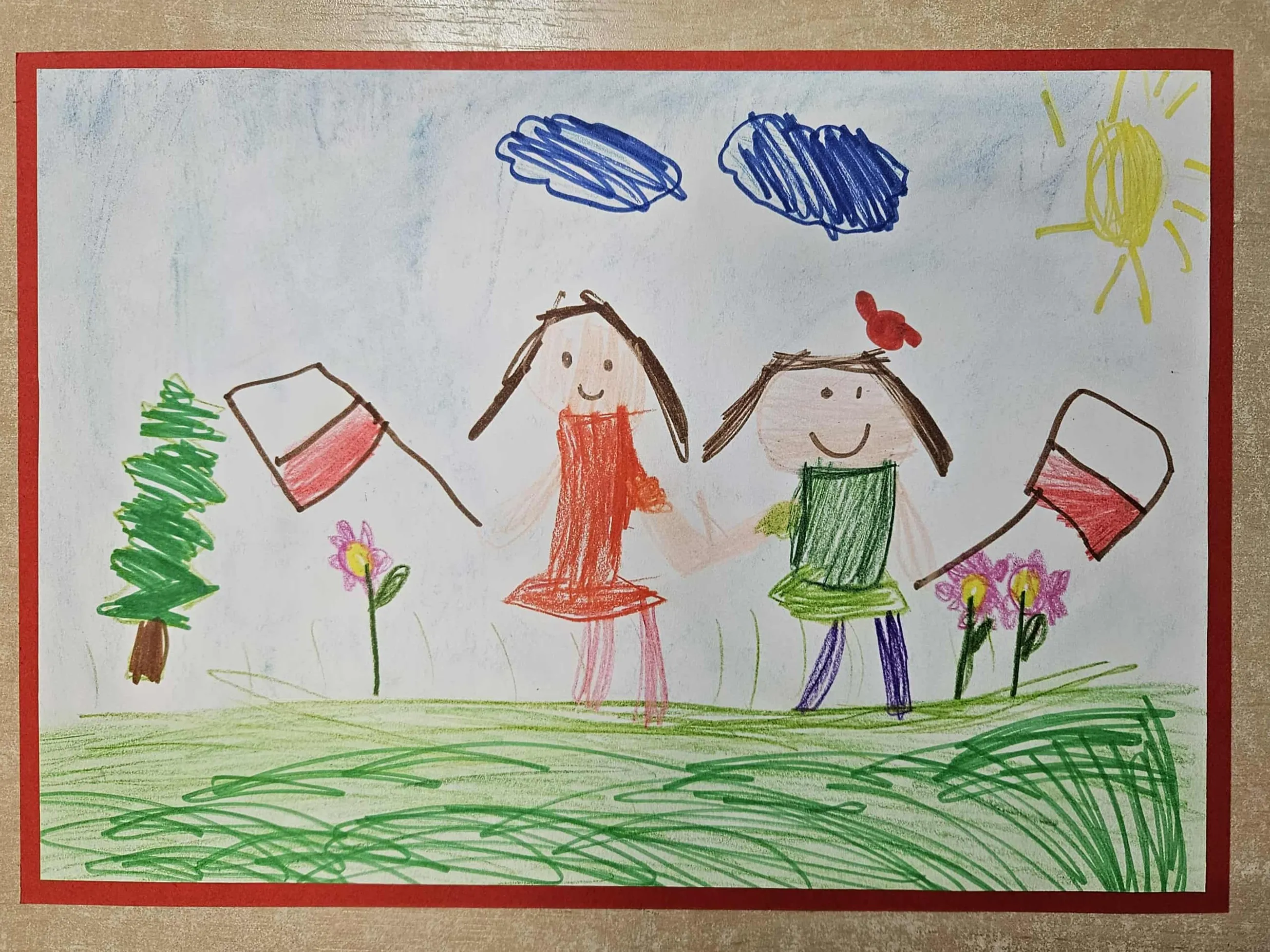 Dwie uśmiechnięte postacie trzymają się za ręce na zielonej łące, każda z nich trzyma flagę Polski. W tle jest zielone drzewo, trzy różowe kwiaty, dwie niebieskie chmury i żółte słońce na niebieskim niebie. Całość jest oprawiona czerwoną ramką.