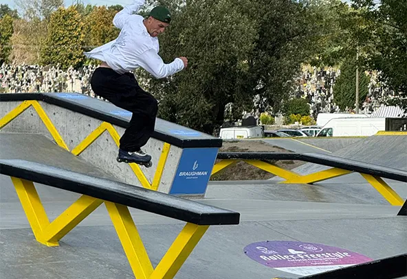 Mężczyzna w białej bluzie i czapce jedzie na rolkach po rampie w skateparku na zewnątrz w ciągu dnia.