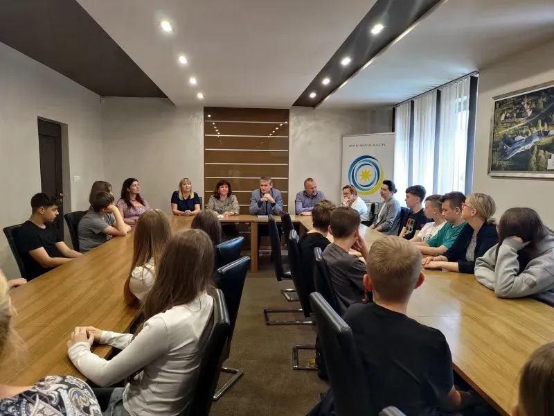 Grupa osób siedzi przy długim stole konferencyjnym w sali spotkań.