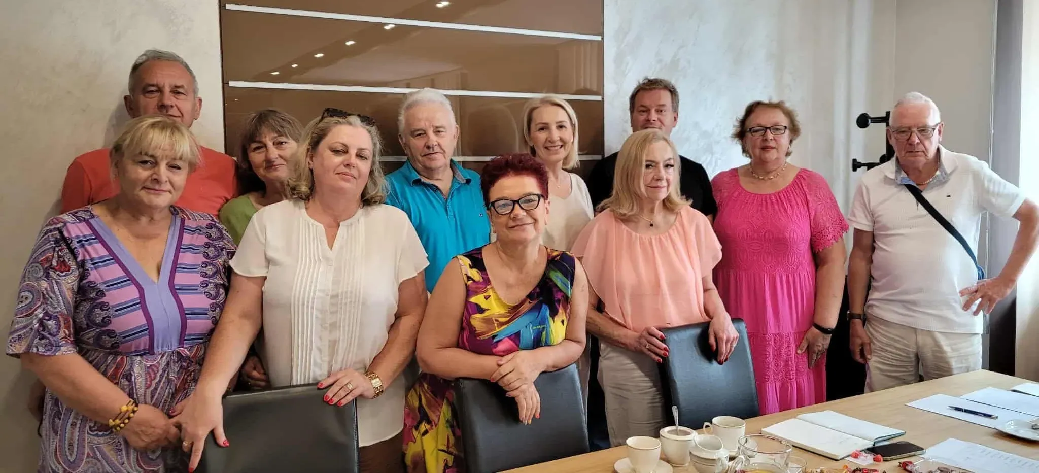 Grupa jedenastu osób stoi w sali konferencyjnej przy stole z kawą, notatnikami i dokumentami.