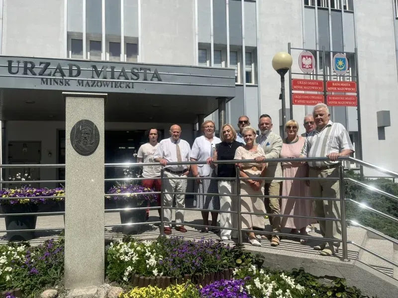 Grupa osób stoi przy barierce przed wejściem do budynku Urzędu Miasta Mińsk Mazowiecki.