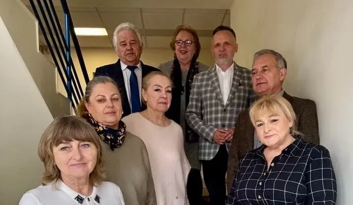 Osiem osób stoi w grupie przy schodach na korytarzu.